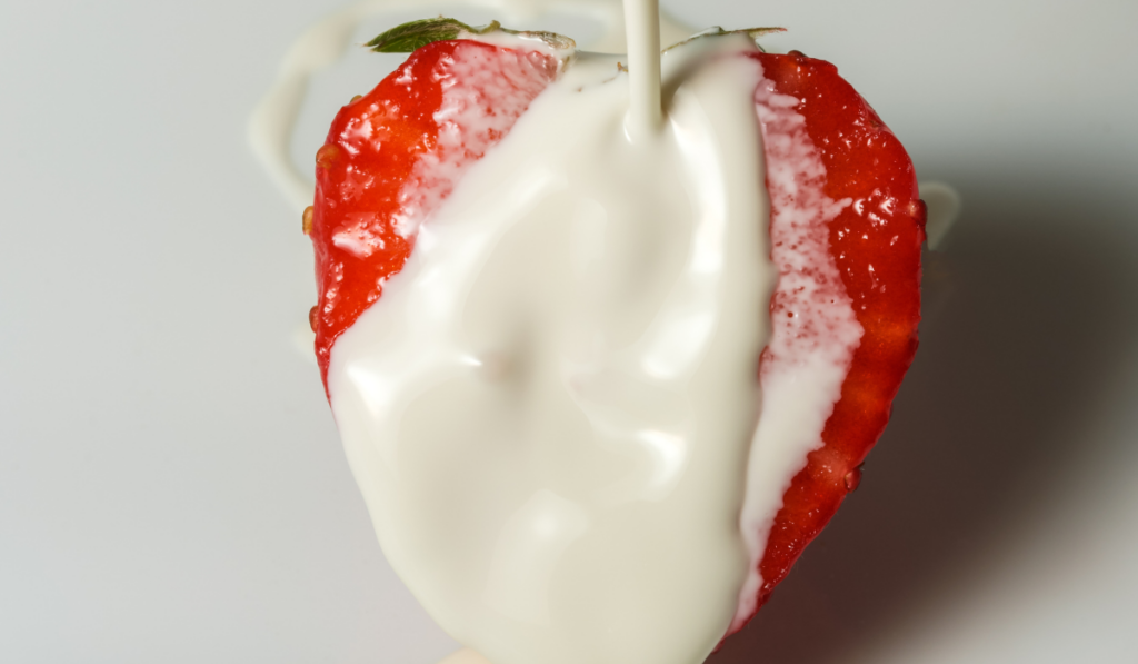 Half ripe sweet strawberries in heavy cream on berry dessert close-up 