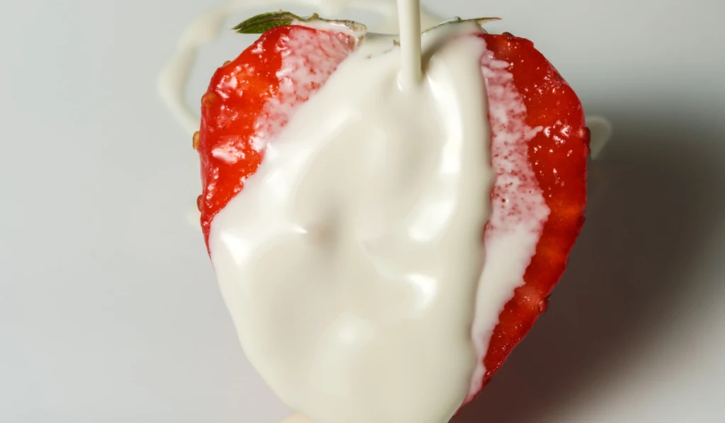 Half ripe sweet strawberries in heavy cream on berry dessert close-up 