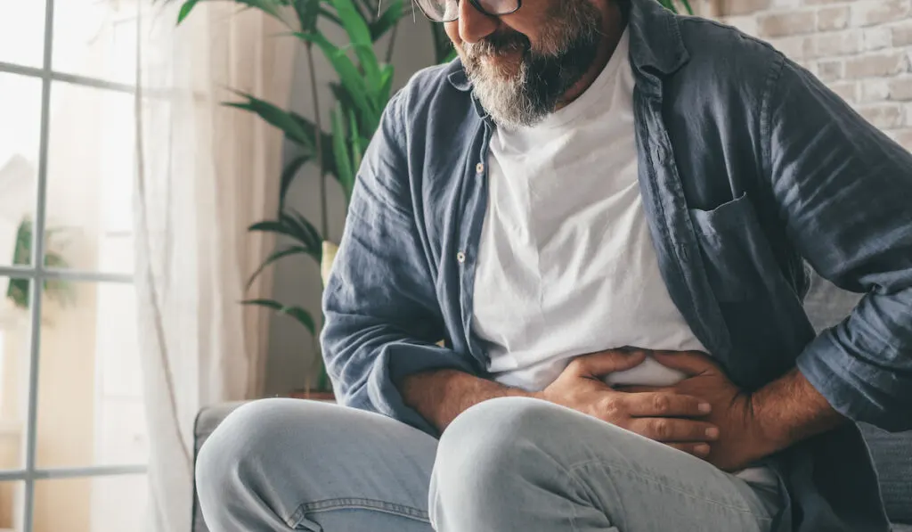 man suffering with stomach pain sitting at home 