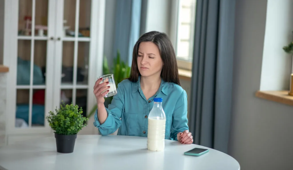 woman disappointed with milks taste, sitting and holding glass of milk at home