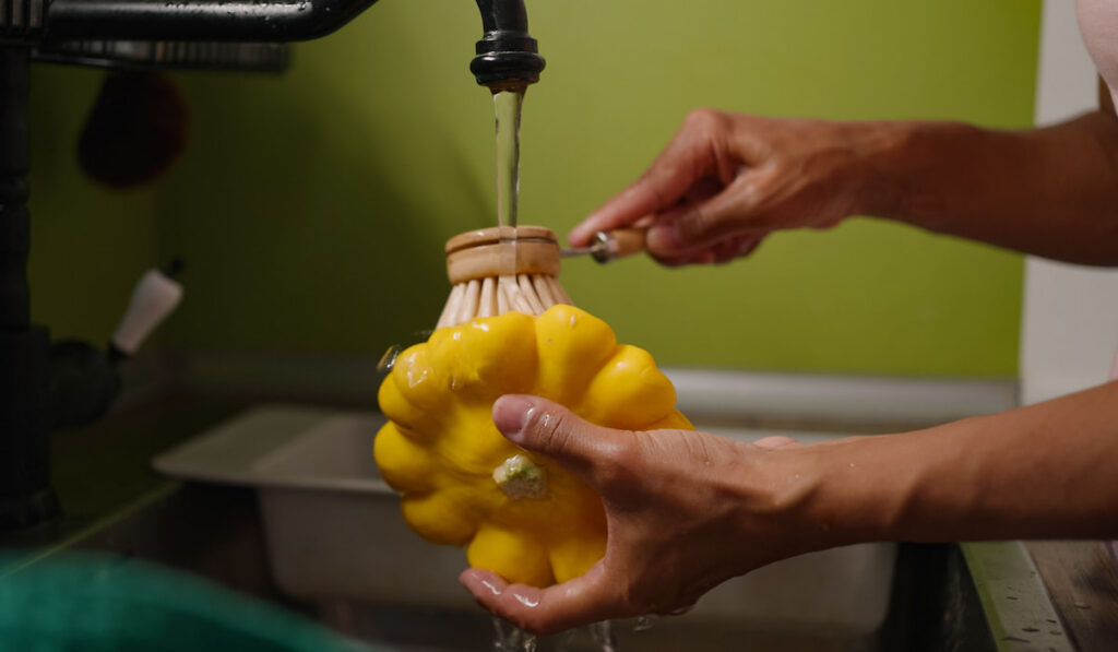 woman washes yellow squash under water running from faucet