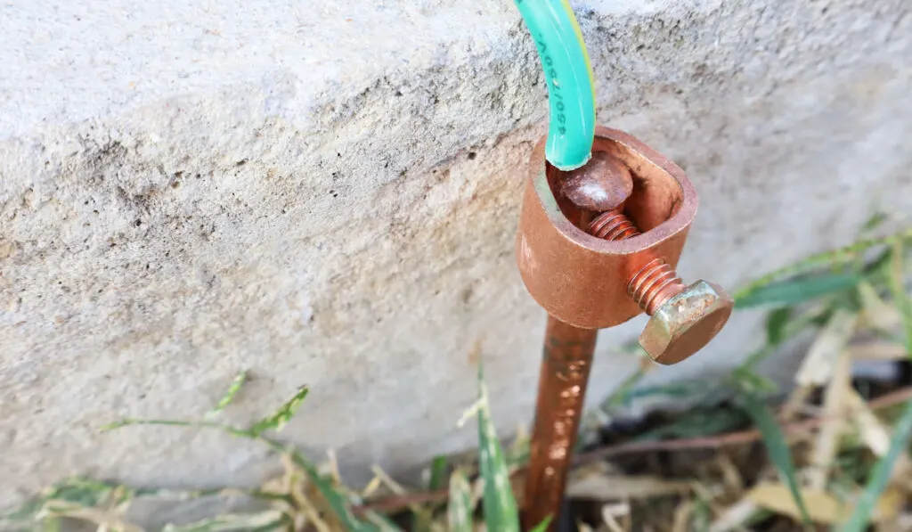 Close-up of copper electriccal groudning rods pinned into the ground beside the cement wall