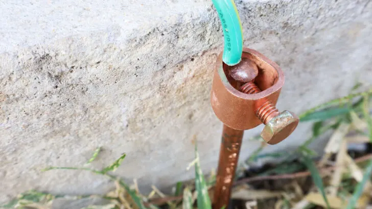 Close-up-of-copper-electriccal-groudning-rods-pinned-into-the-ground-beside-the-cement-wall