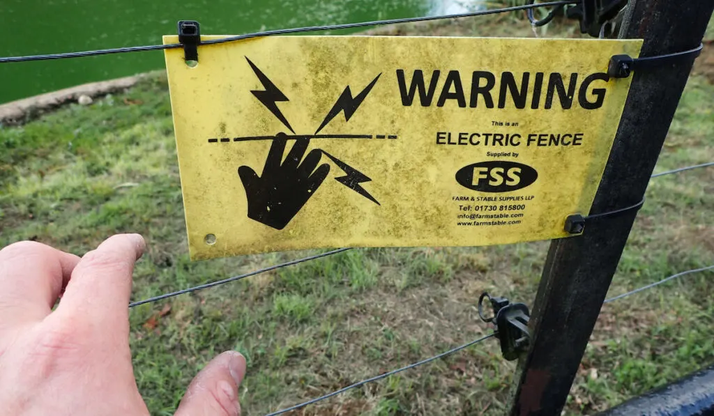 Hand about to touch an electric fence with a yellow electrical warning danger sign