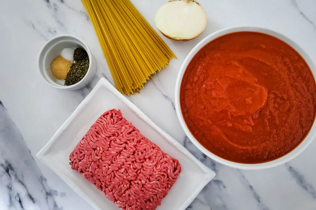ingredients for a spaghetti with meat sauce; tomato sauce, ground beef, pasta, herbs and spices on  the table