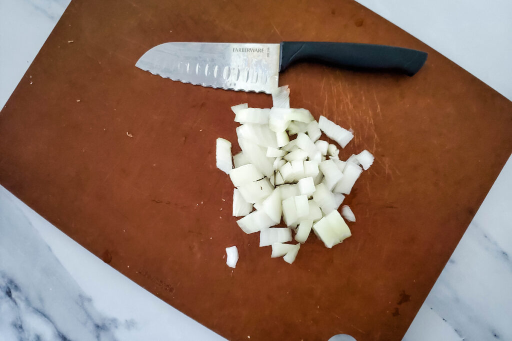 diced onion on a brown chopping board and a knife