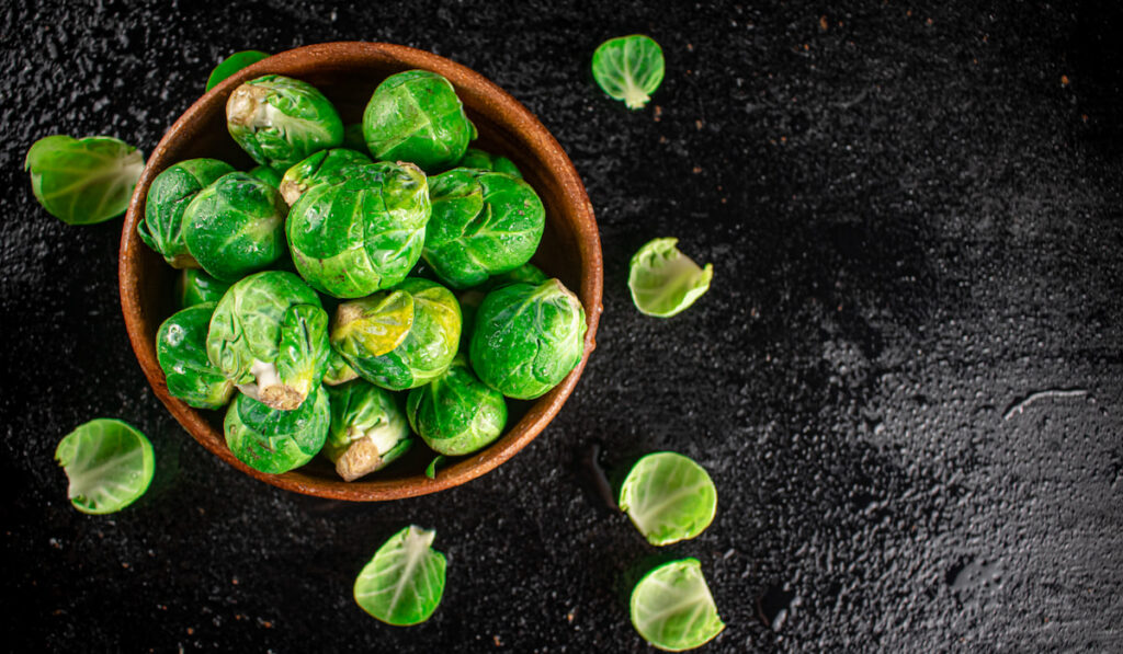Fresh brussels sprouts in a wooden bowl on a black background
