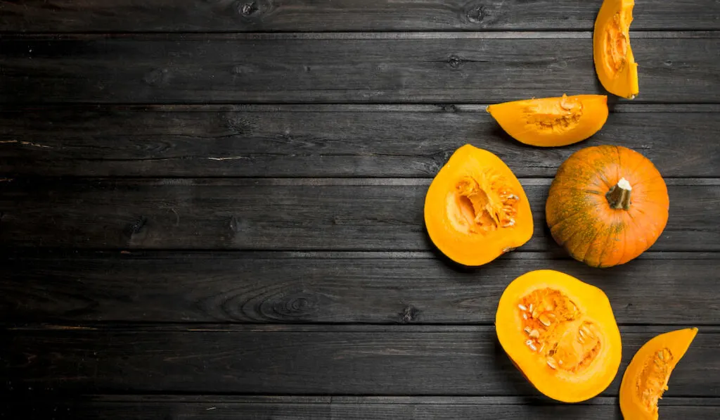 Whole and sliced fresh pumpkin on dark wooden background