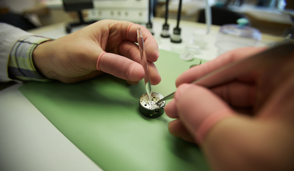 watchmaker in finger gloves using tweezers and lubricating watch