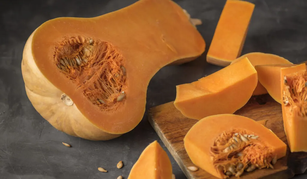 Butternut squash sliced on a cutting board on dark stone background