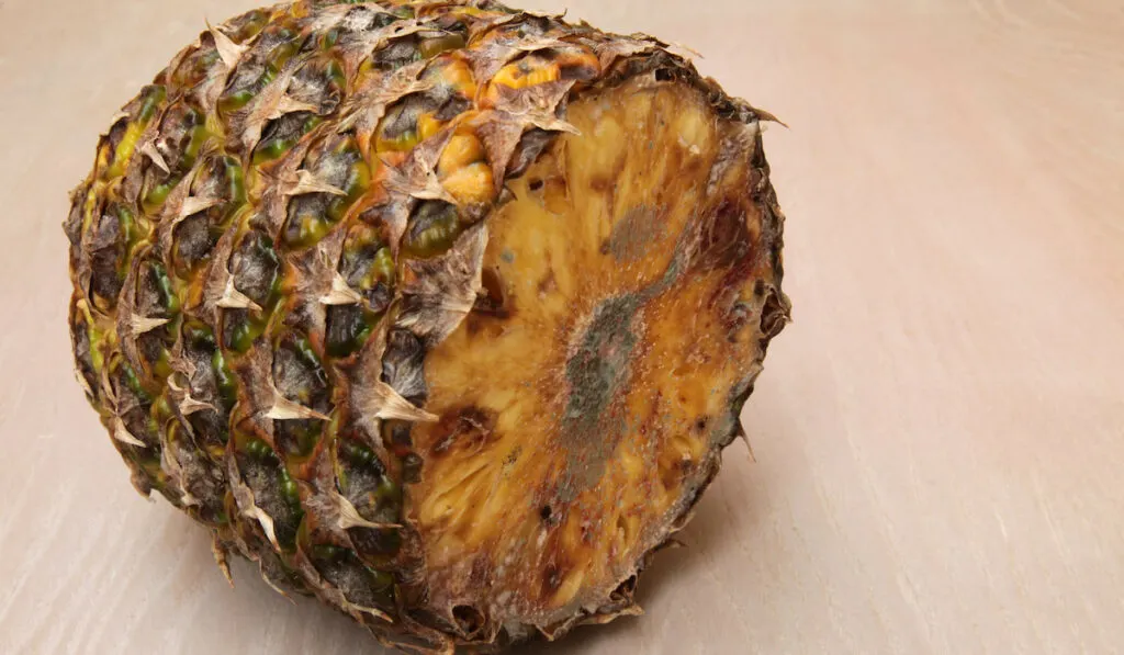 Cut pineapple with putrid surface on wooden table