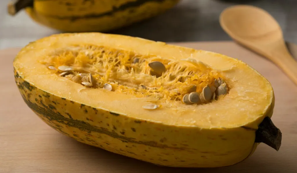 Halved raw spaghetti squash on wooden board