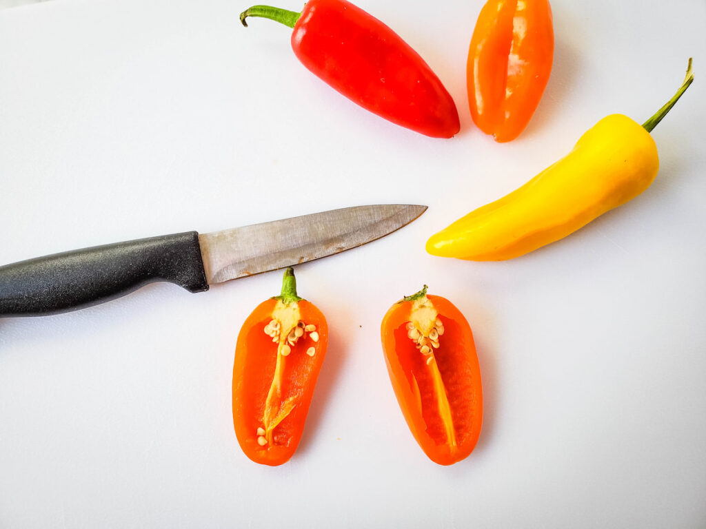 Sliced and whole bell peppers and knife on white background