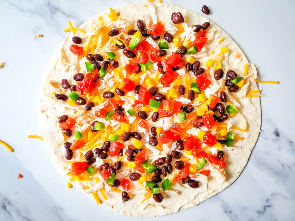 Sprinkled chicken, tomato, black beans, corn and jalapeño on a tortilla on marble background