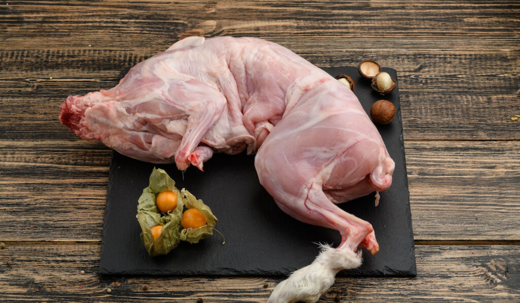 Whole raw rabbit meat with spices on black board on wooden table