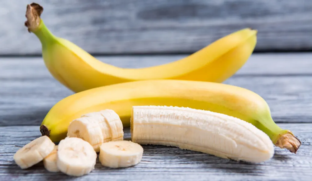 peeled, sliced and whole bananas on gray wooden background