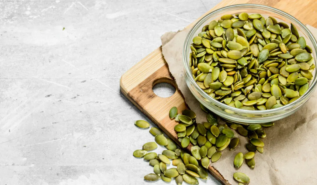 pumpkin seeds in a glass bowl on wooden board