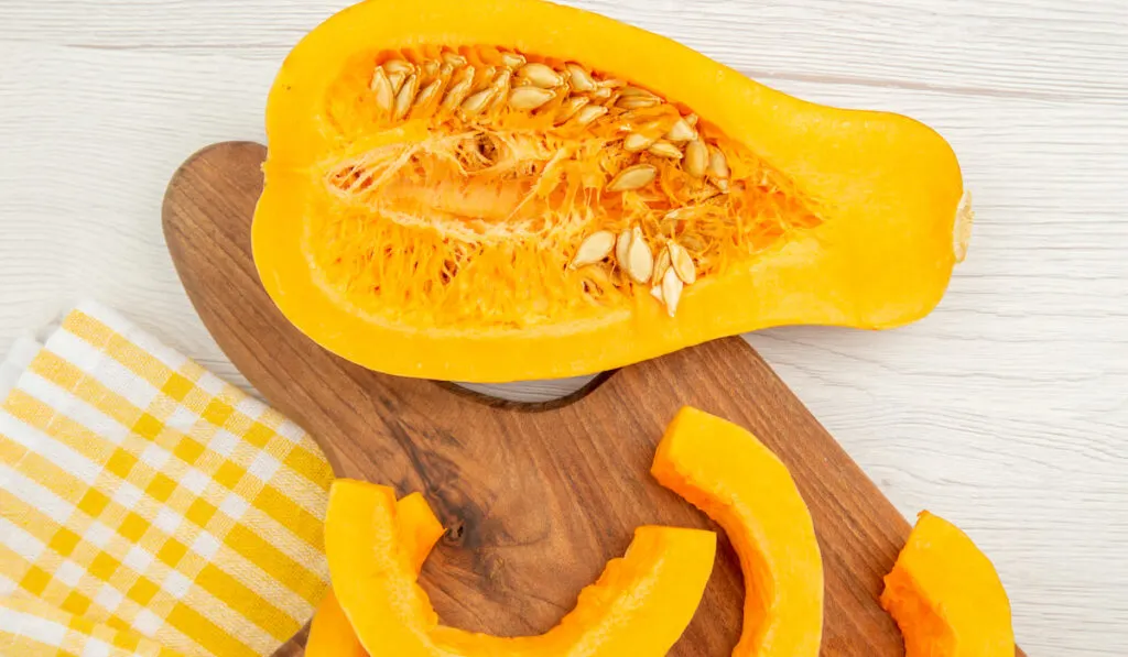 sliced butternut squash on chopping board with yellow white checkered fabric on the table