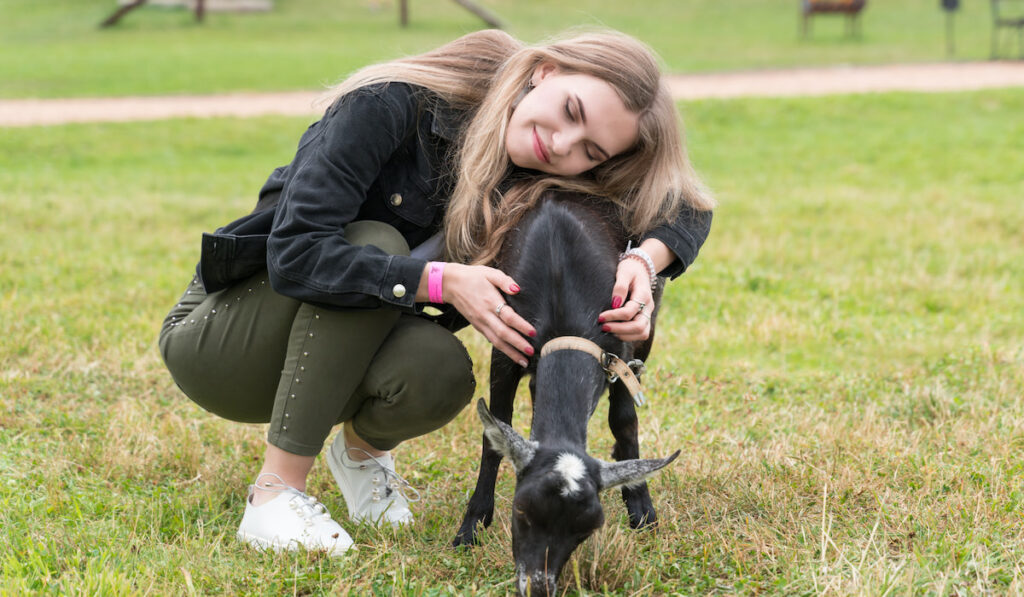 Happy young girl hugging black goat 