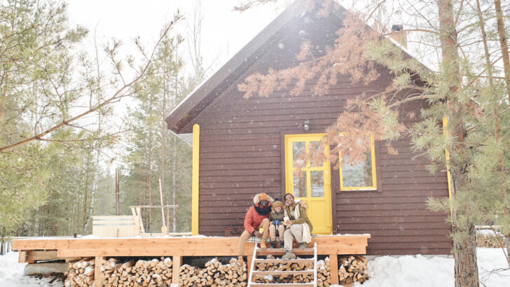 happy family of three sitting on porch by their cottage in the forest in winter