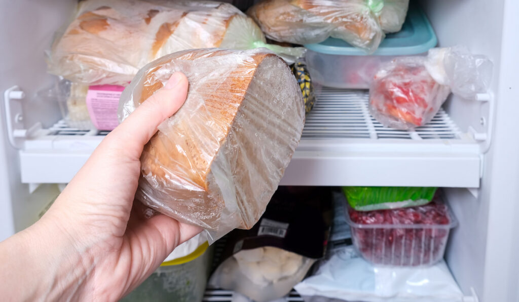 A hand putting a package of brown bread in reserve on a shelf of a home freezer