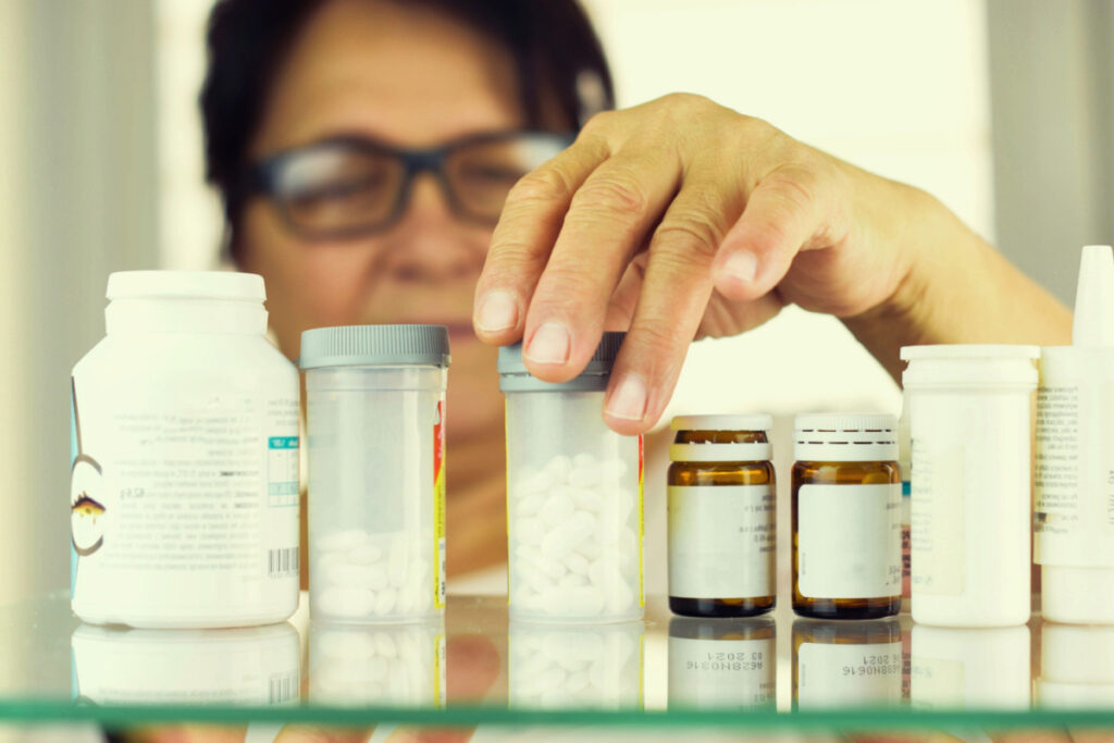 An elder woman organizing medicine bottles inside a medicine cabinet