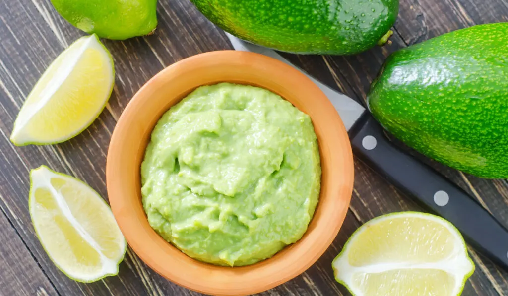 Avocado puree in wooden bowl with lemon and fresh avocado on the table