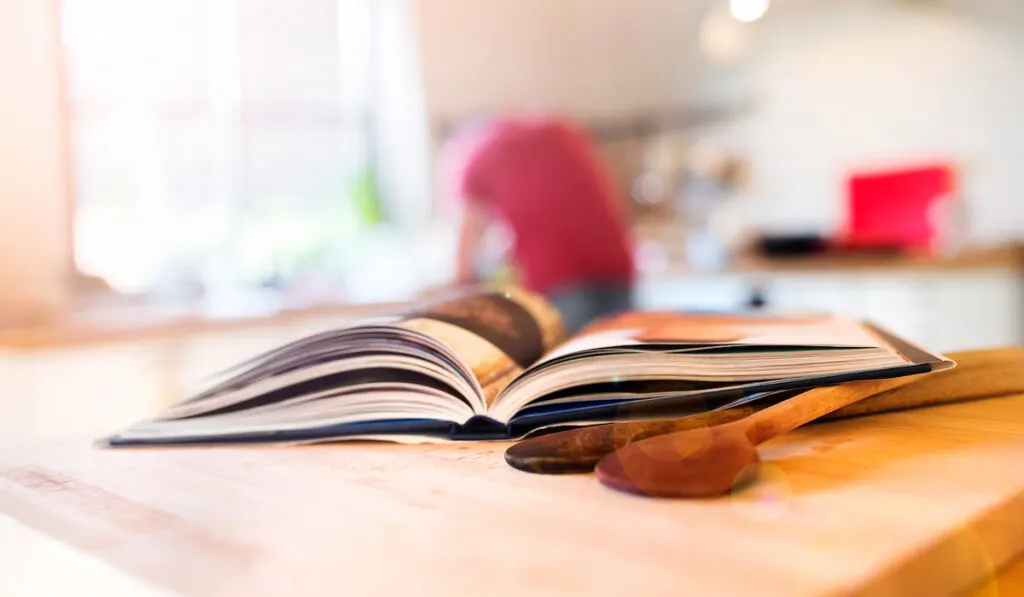 Cook book laid on a kitchen table with two wooden spoons