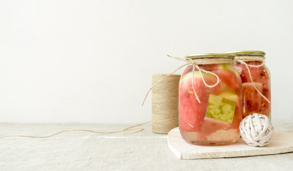 Fermented preserved watermelon in glass jar on white rustic background