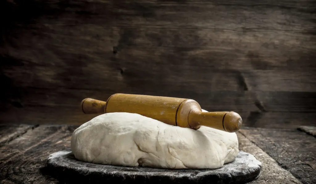 Fresh dough with rolling pin. On a wooden background