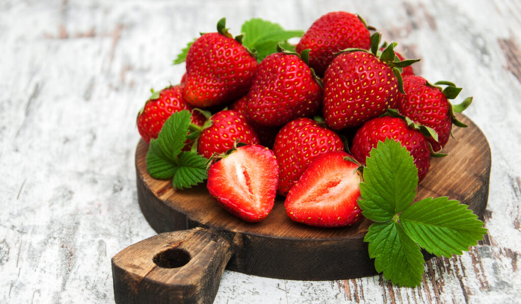 Fresh strawberries with leaves on wooden board on the table