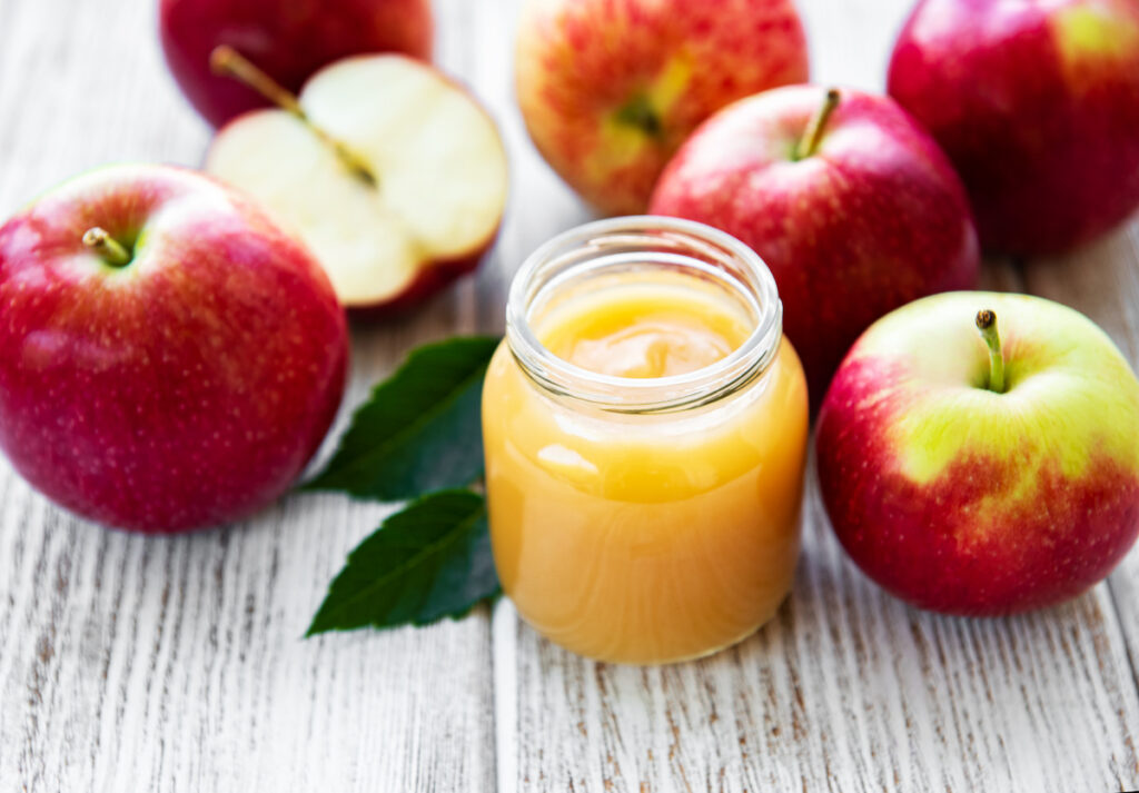 Freshly made applesauce in a small glass jar surrounded by red apples