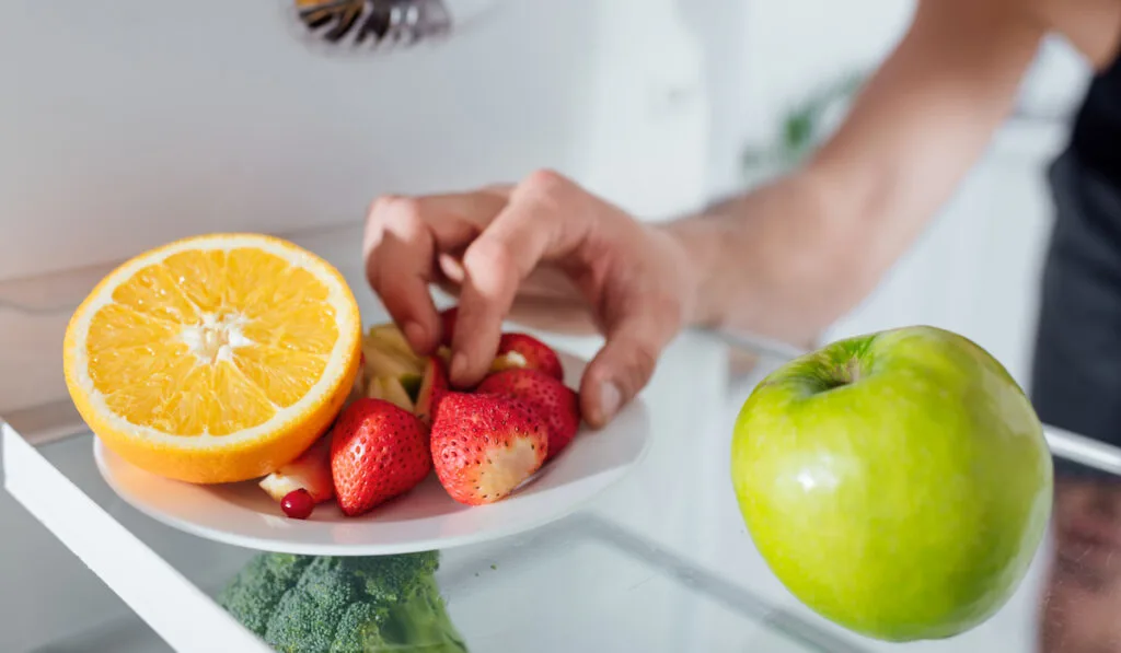 man taking a strawberry from a plate of fruit in the fridge