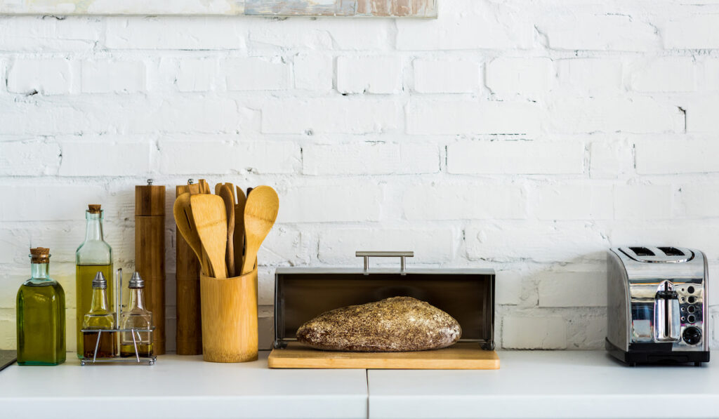 Open breadbox with a bread and toaster and kitchen utensils on kitchen counter