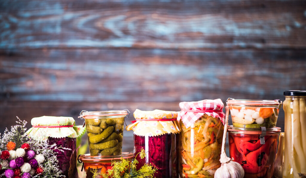 Preserved food, marinated fermented and pickled vegetables in jars on wooden background