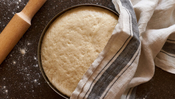 raw yeast dough resting and rising in large metal bowl covering with linen towel