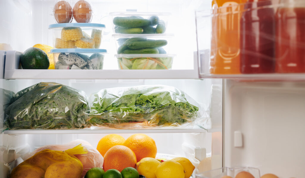 Refrigerator full of groceries including fresh greens, citrus fruits, vegetables like cucumber and eggs