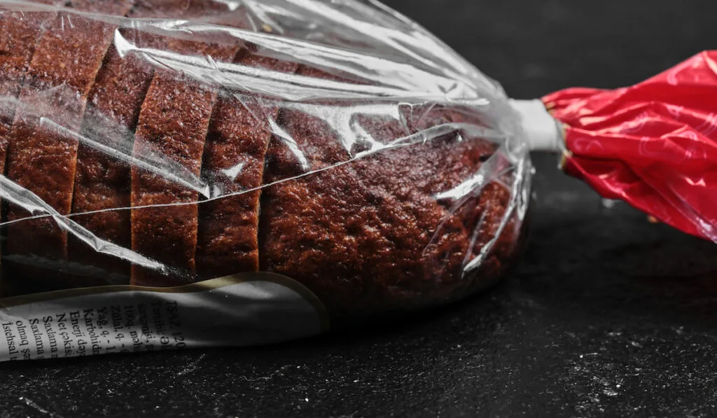 Sliced black rye bread in plastic bag on dark background