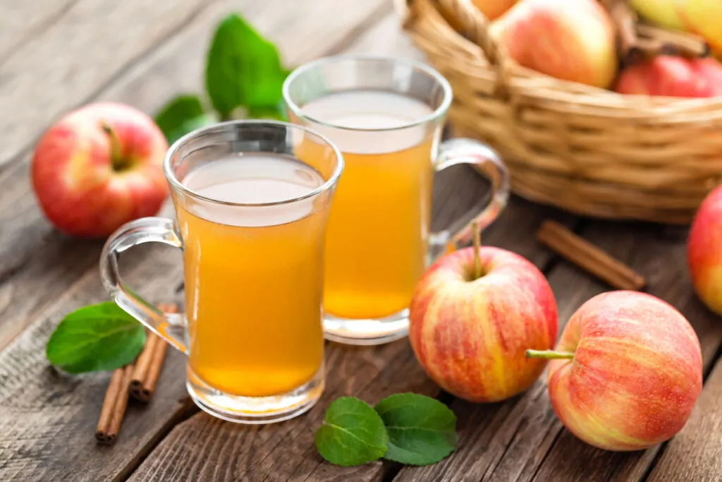 Two cups of freshly squeezed apple cider on top of a wooden table