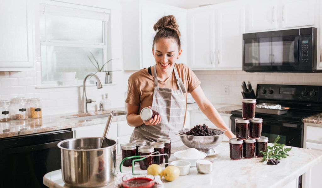 Woman canning homemade blackberry jam in white kitchen
