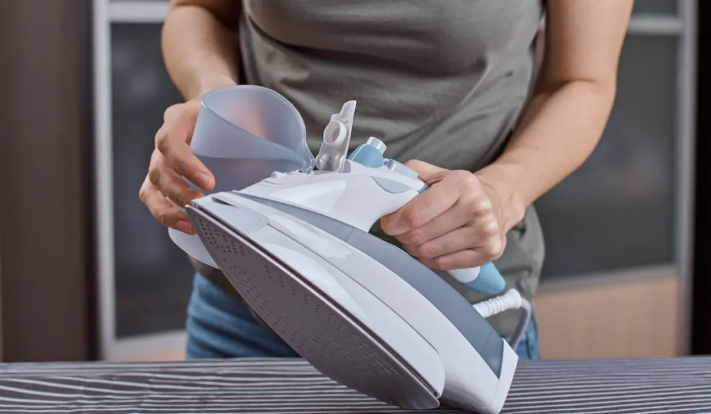 woman adding water in an iron to remove carpet stains