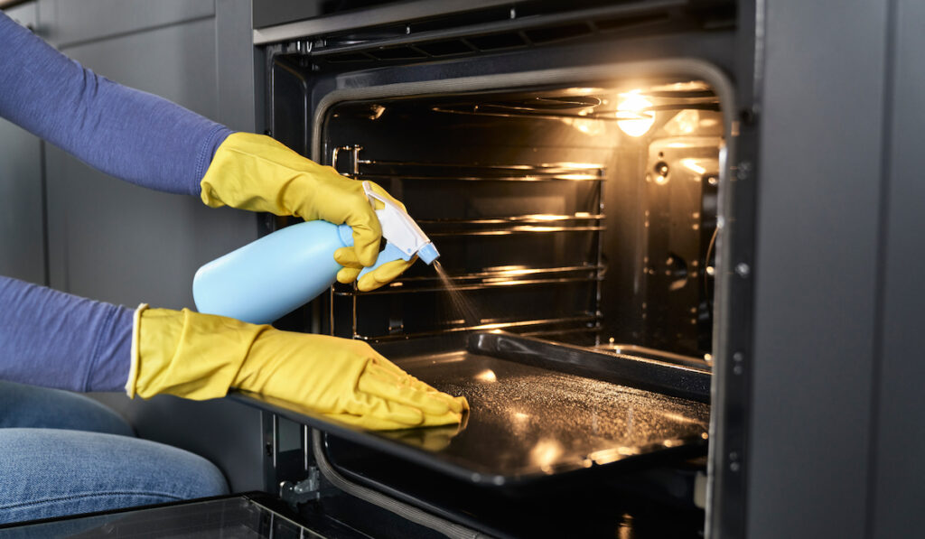 Woman spraying liquid cleaning in oven tray at home