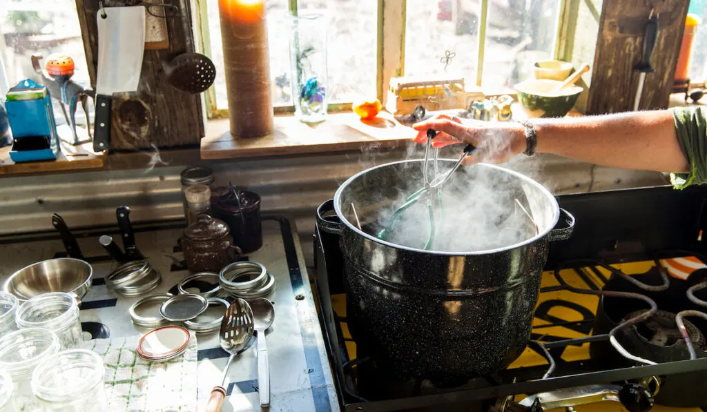 Woman using tongs to remove preserves jar from steaming saucepan

