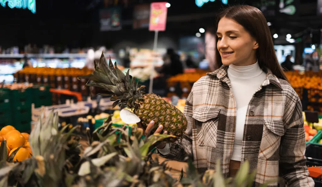 Young woman choosing pineapple during shopping at supermarket