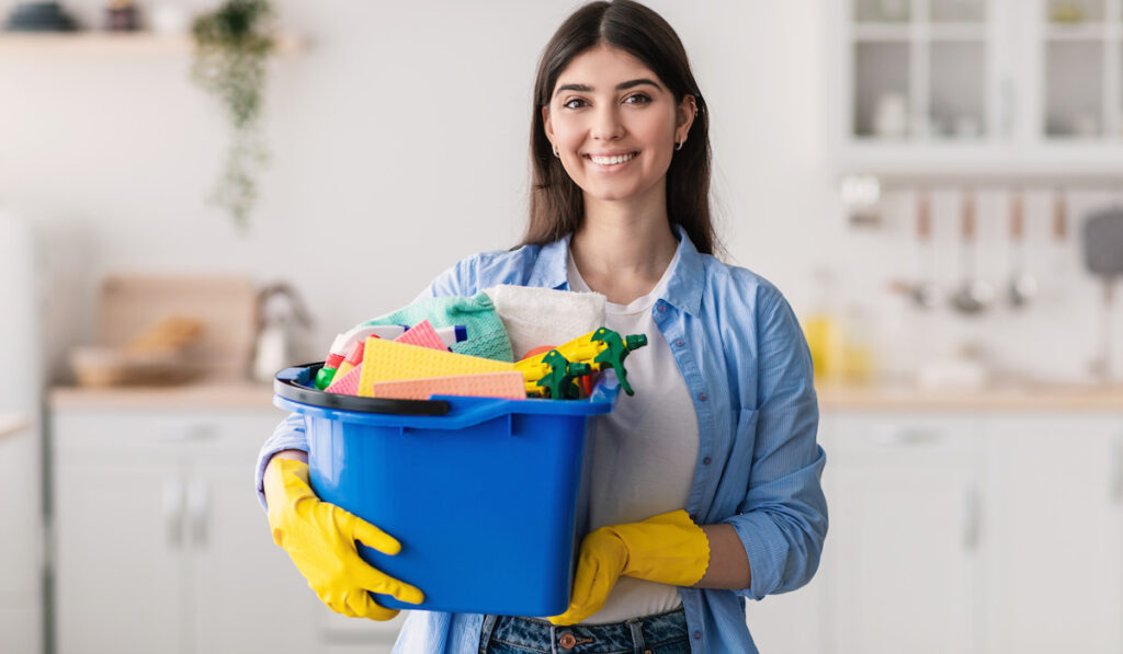 Young woman holding bucket with cleaning supplies tools in the kitchen