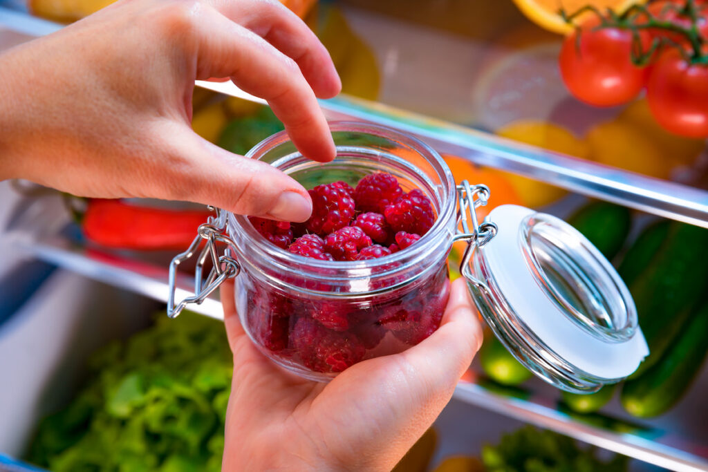 a girl putting a small jar of raspberries inside the fridge