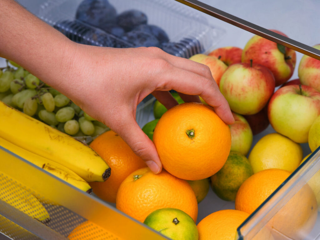 a woman storing oranges inside the fridge