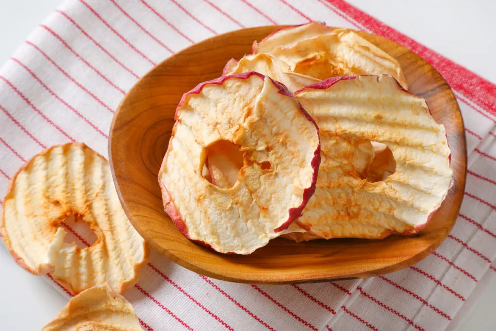 dried apples slices in a wooden bowl on top of a cloth