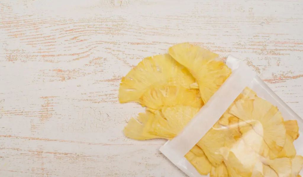 dried (dehydrated) pineapple slices coming out from plastic bag on wooden table