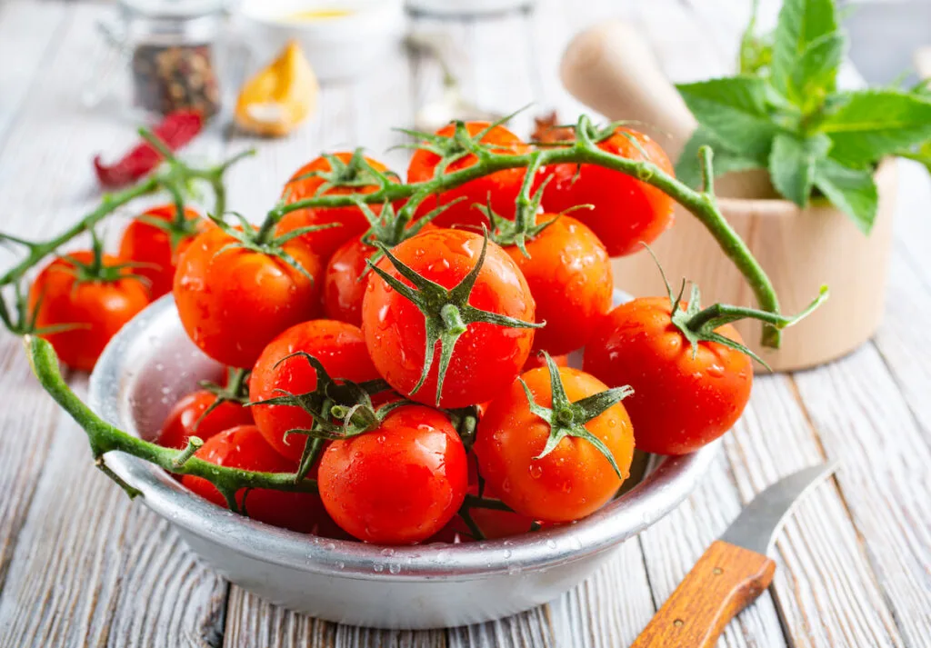 fresh tomatoes in a stainless bowl beside a small knife